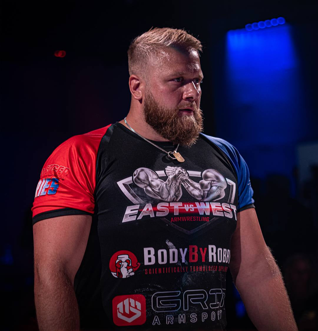 Man wearing a raglan all ove print t-shirt with various logos and text, standing in a dark setting.