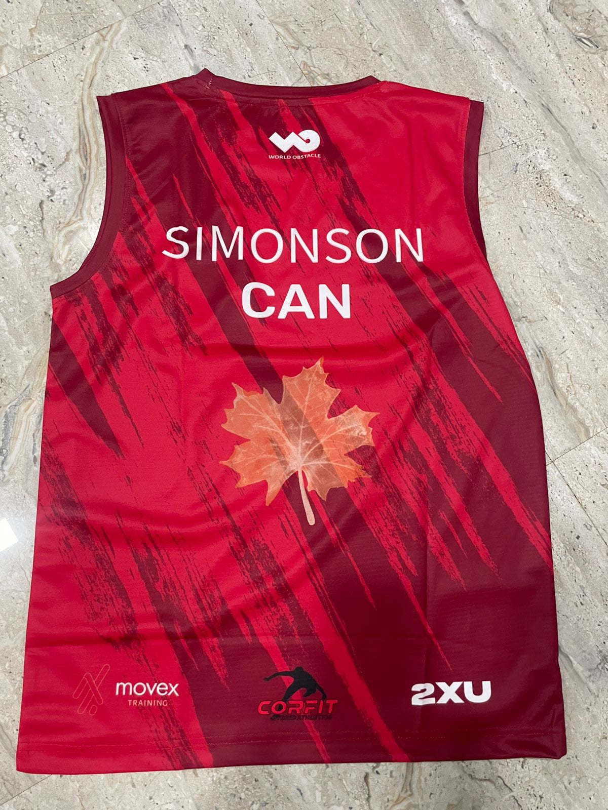 Red sports jersey with a maple leaf and branding on a light gray surface