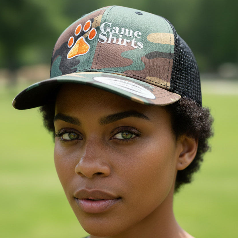 Camouflage baseball cap with paw print and 'Game Shirts' logo on grass