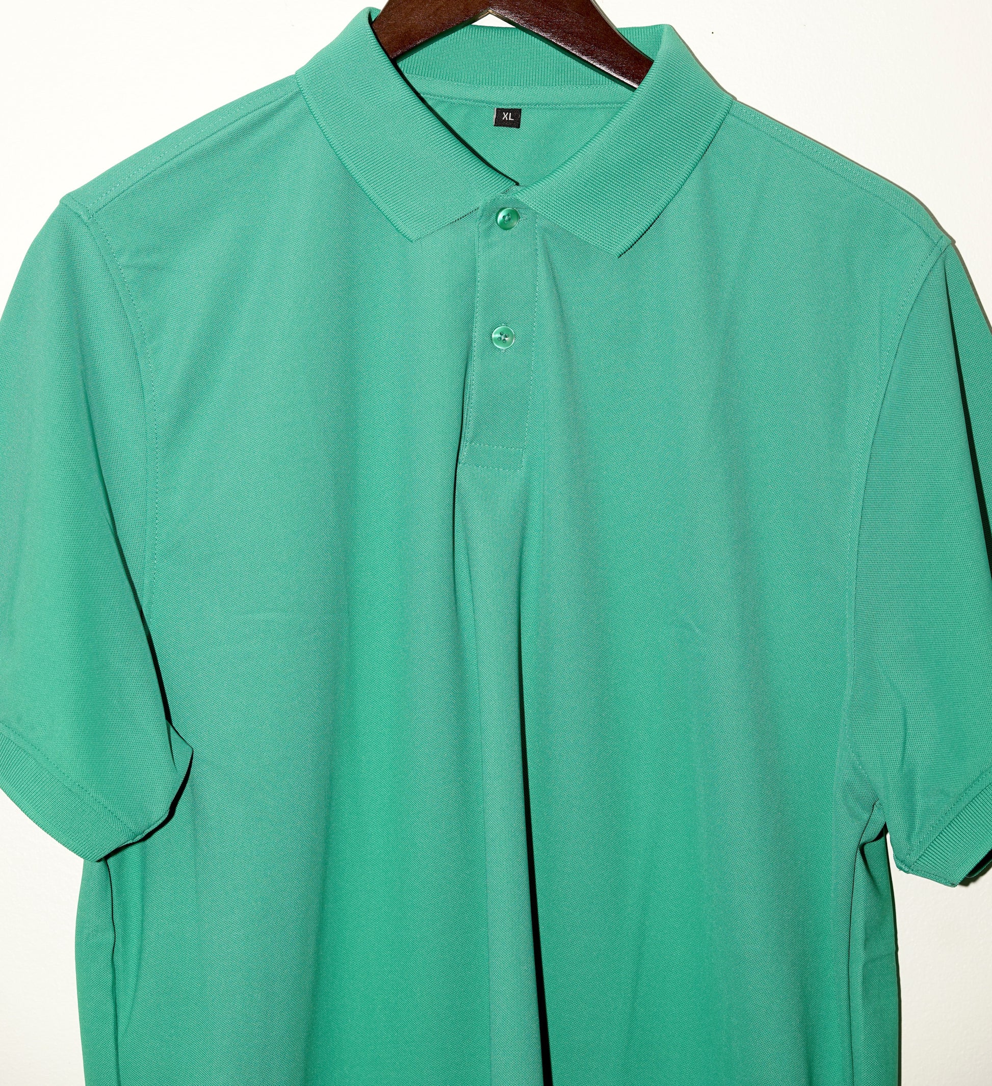 Green polo shirt on a hanger against a white background