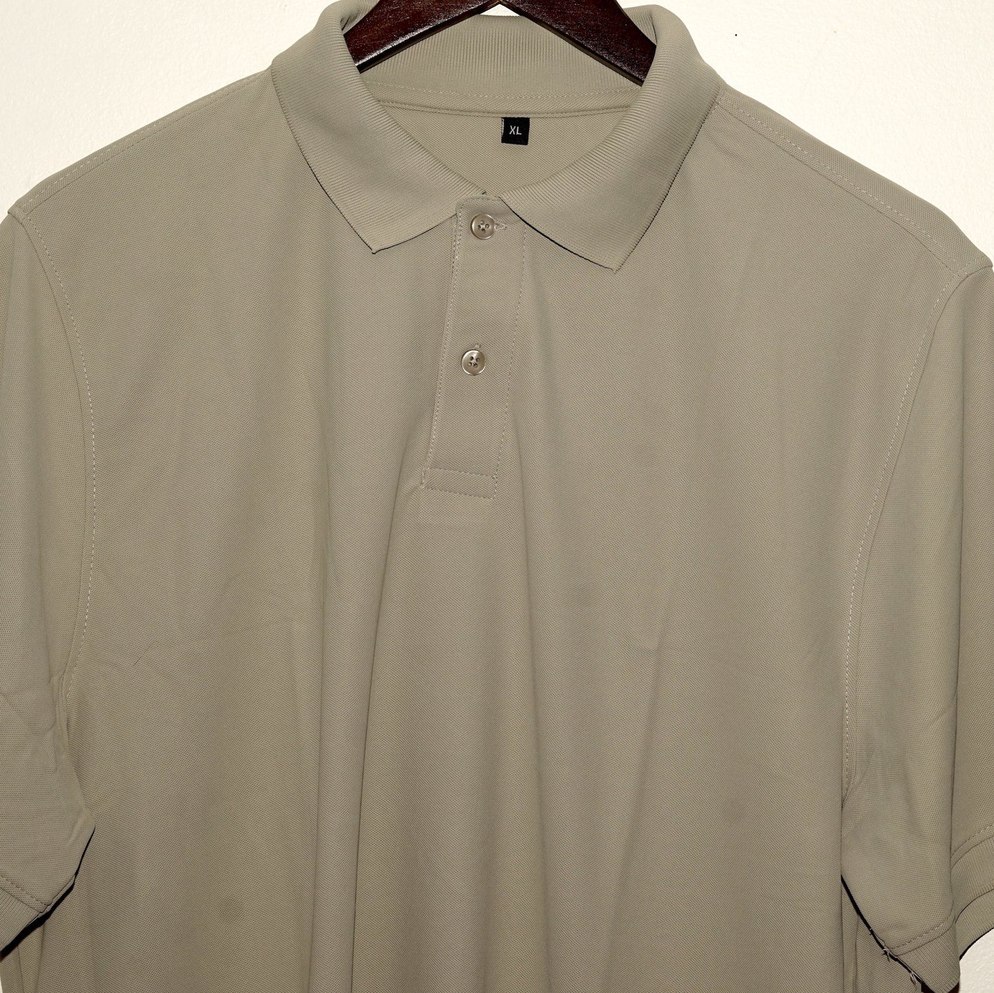 Beige polo shirt on a hanger against a plain background