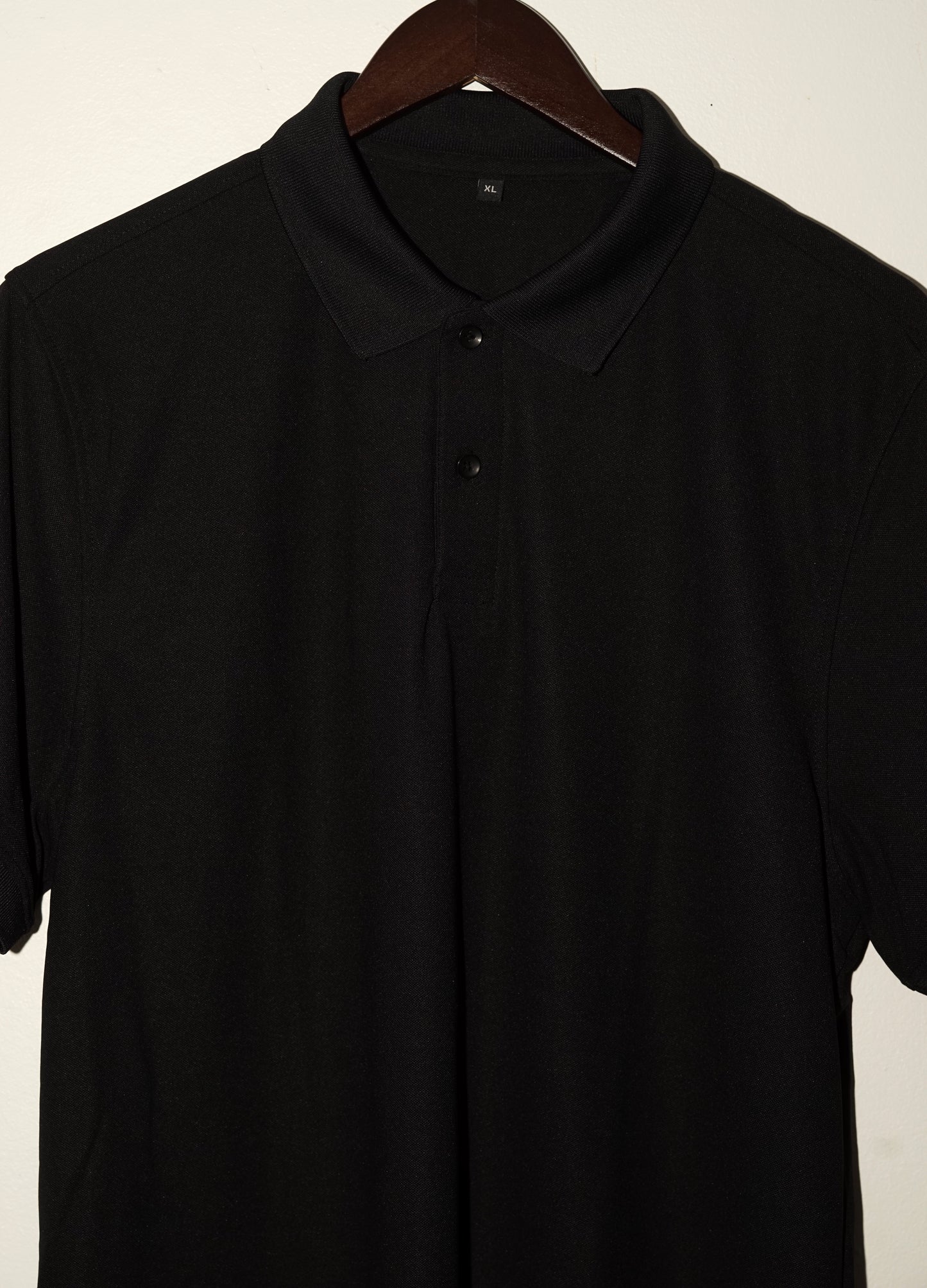 Black polo shirt on a wooden hanger against a plain background