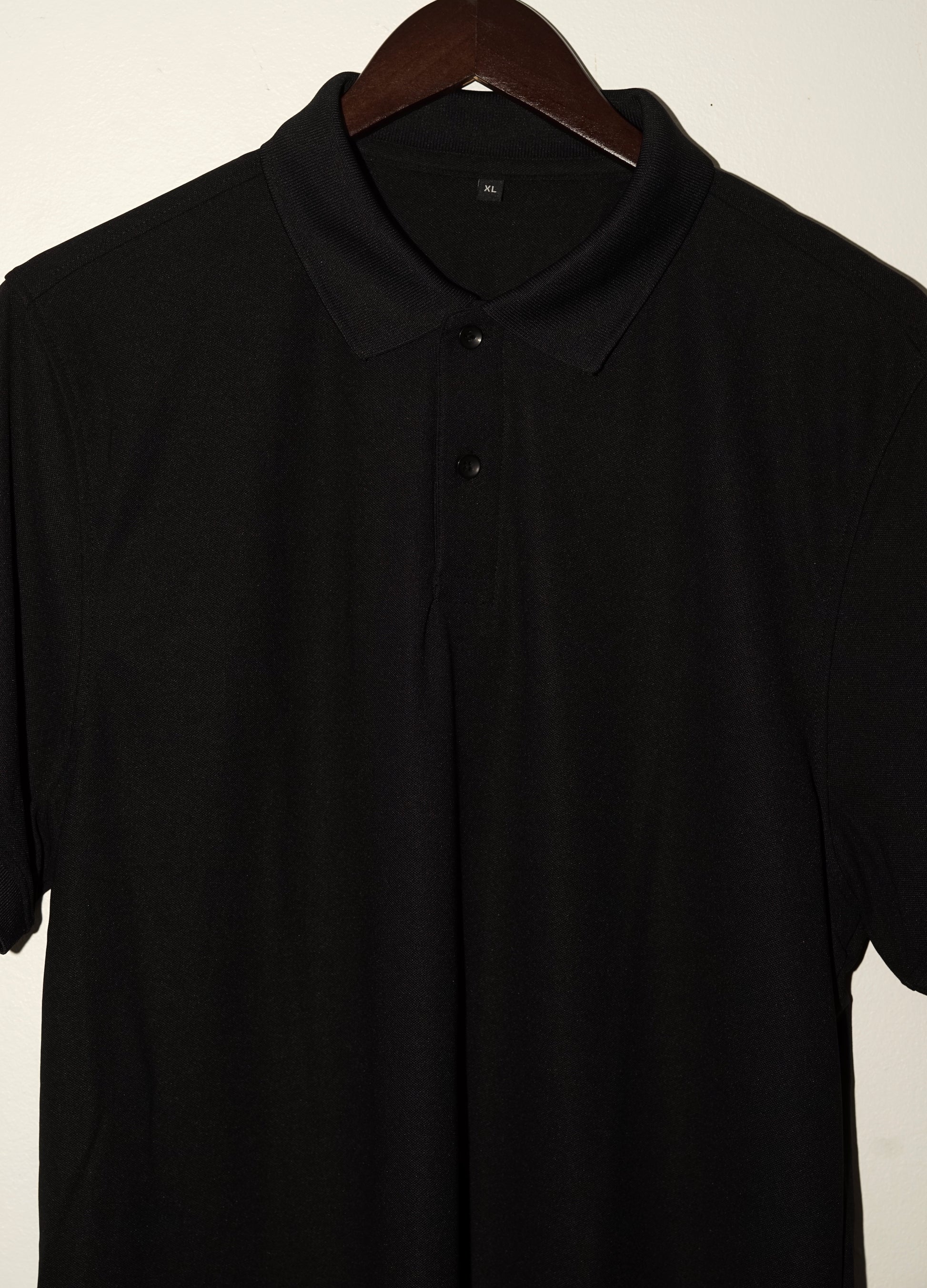Black polo shirt on a wooden hanger against a plain background