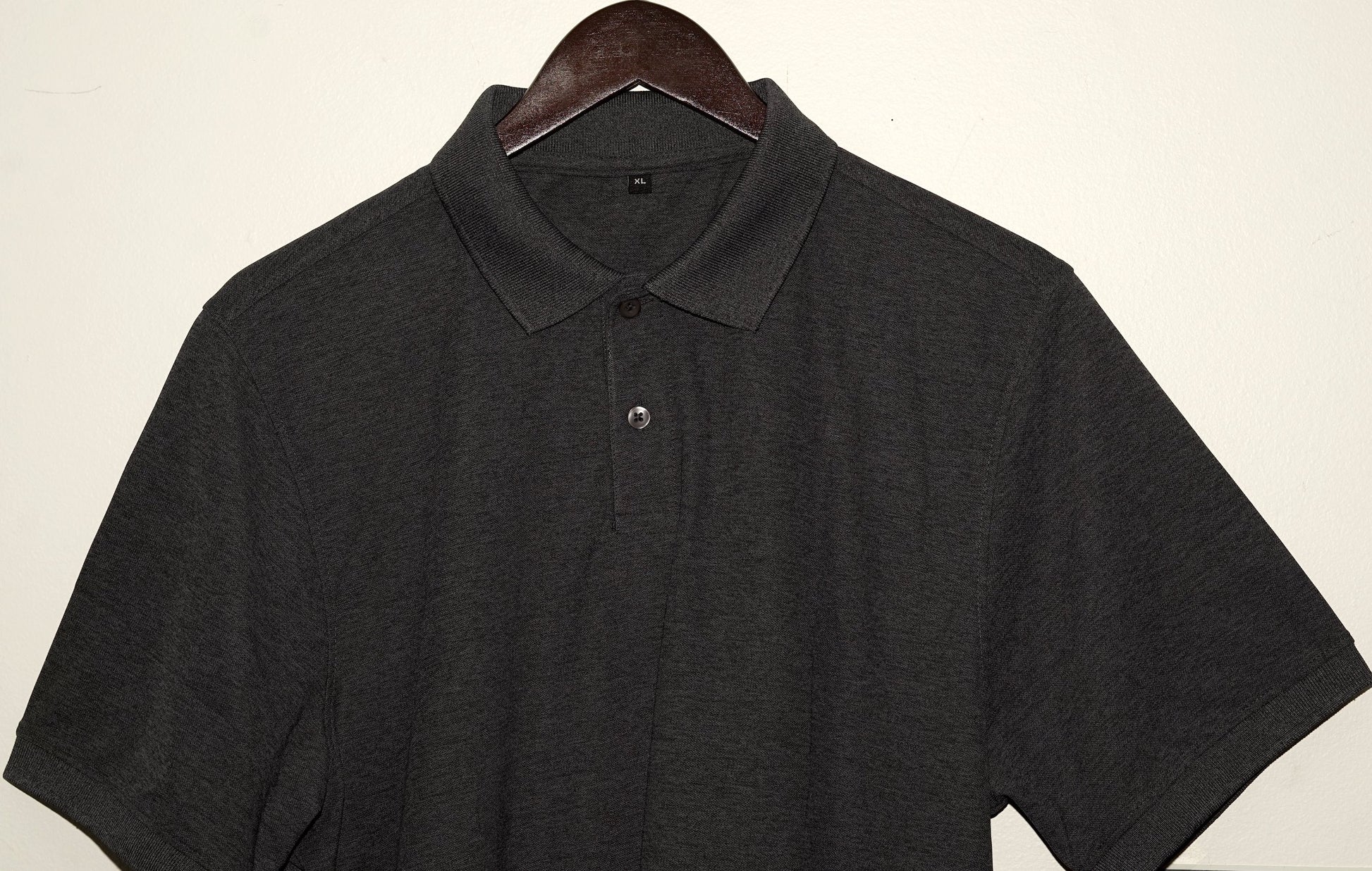 Dark gray polo shirt on a hanger against a plain background